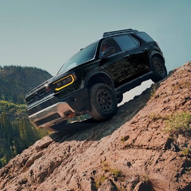 2027 Honda Passport TrailSport Elite in Crystal Black Pearl front driving up a steep rocky mountain slope (Mid-Size SUV).